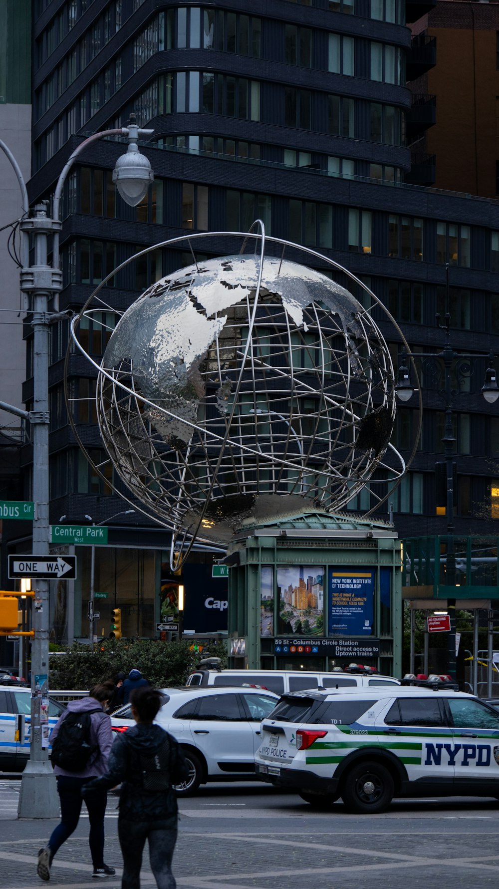 two people walking across a street in front of a globe