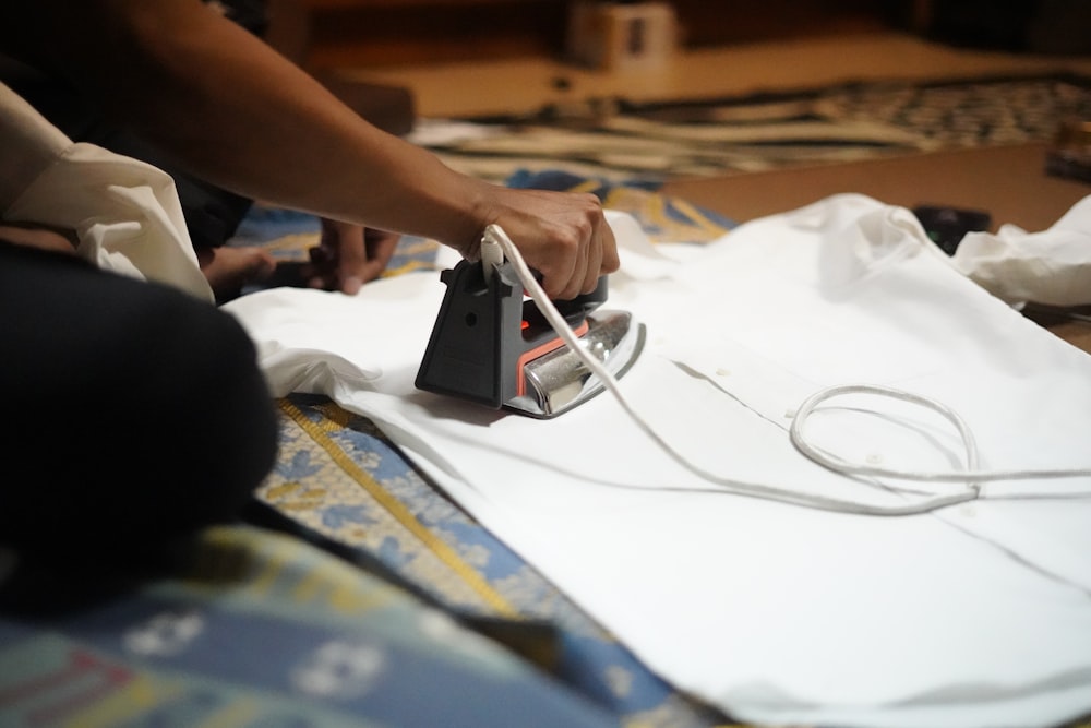 a person ironing a white shirt with a black iron