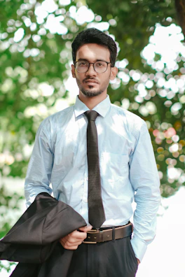 a man wearing glasses and a tie standing in front of a tree