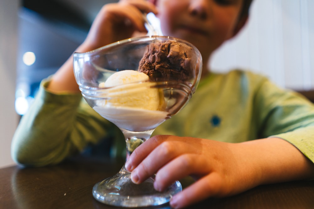 a young boy sitting at a table with a glass of ice cream