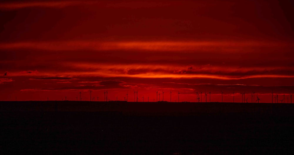 a red sky with a line of windmills in the distance