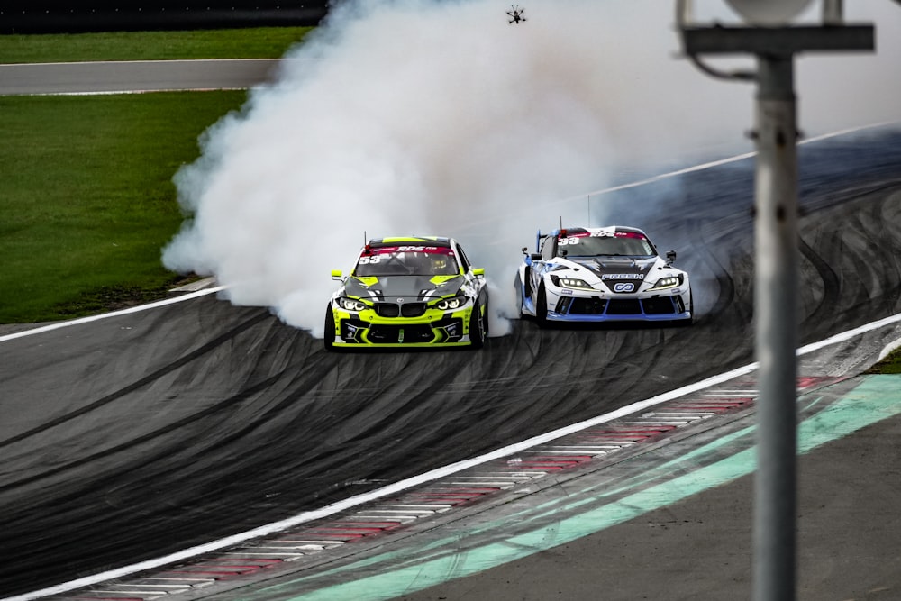 two racing cars on a race track with smoke coming out of the tires