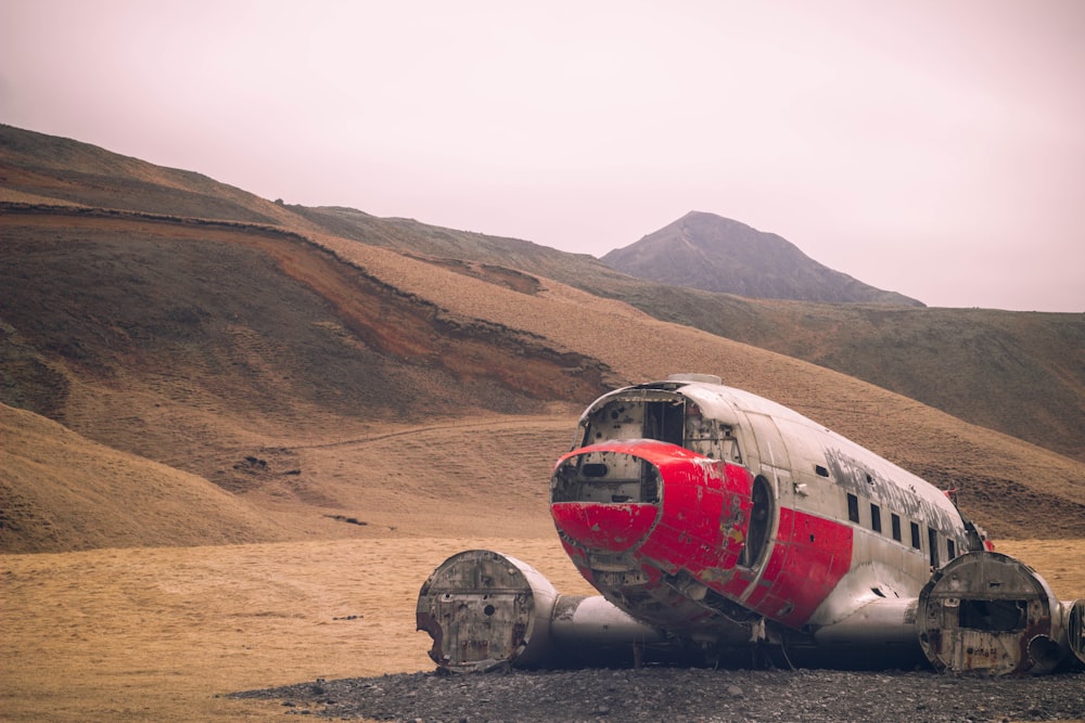 a red and white airplane sitting on top of a dirt field