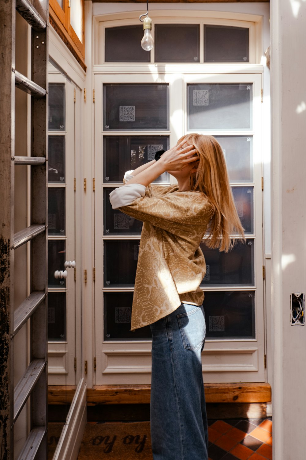 a woman standing in front of a window with her hands on her head