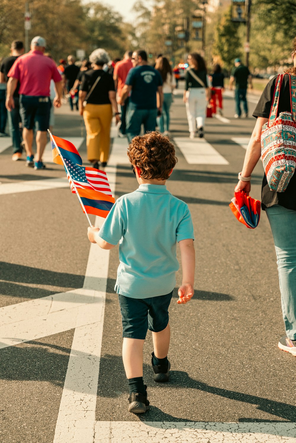 a little boy walking down a street holding a flag
