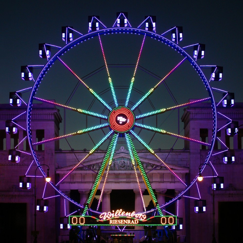 a ferris wheel lit up at night in front of a building