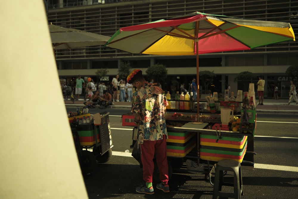 um homem em pé sob um guarda-chuva colorido ao lado de um carrinho