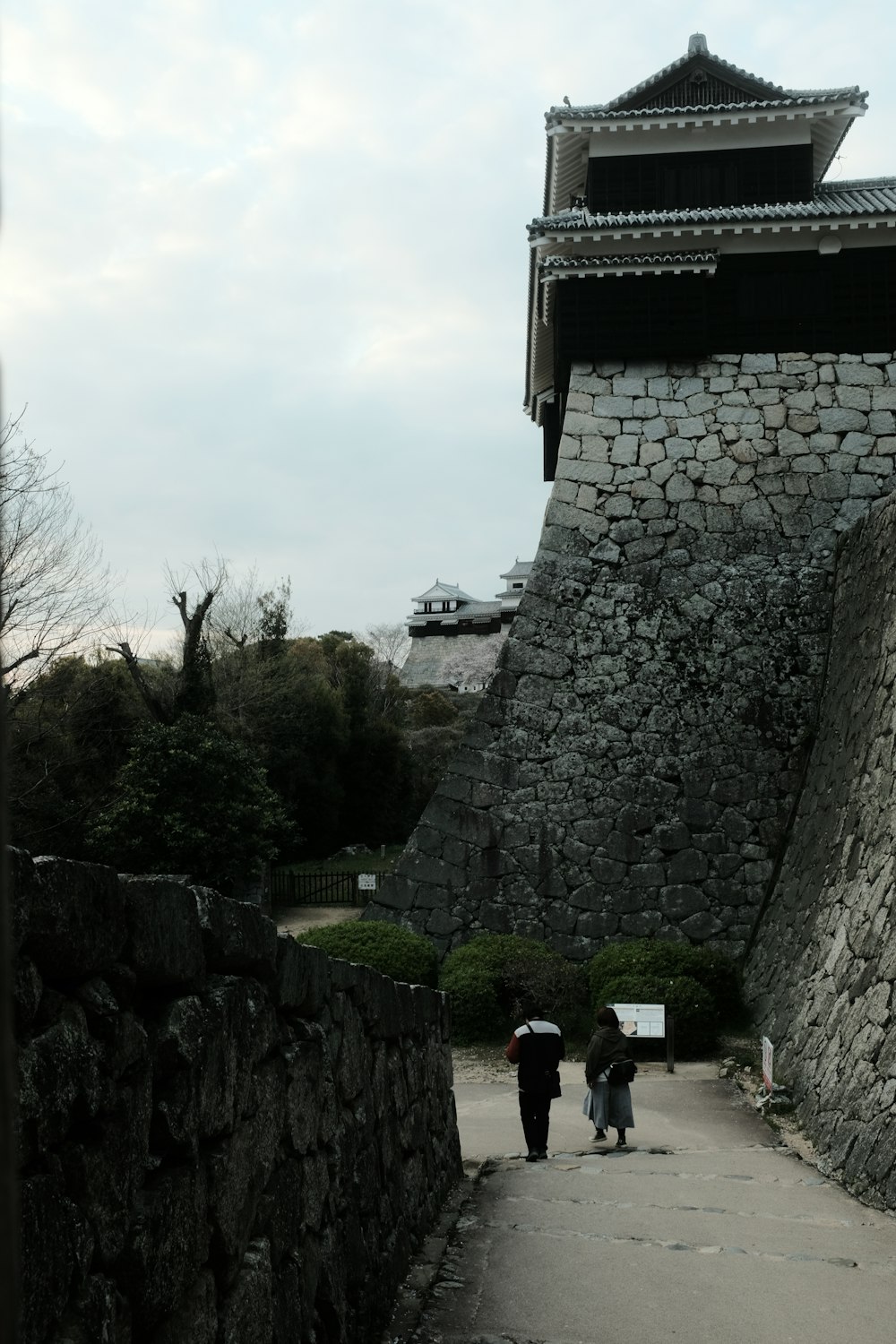 a couple of people walking down a street next to a stone wall