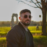 a man wearing sunglasses standing in front of a tree