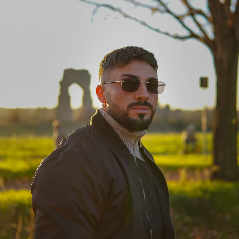 a man wearing sunglasses standing in front of a tree