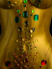a close up of a gold dress with green and red jewels