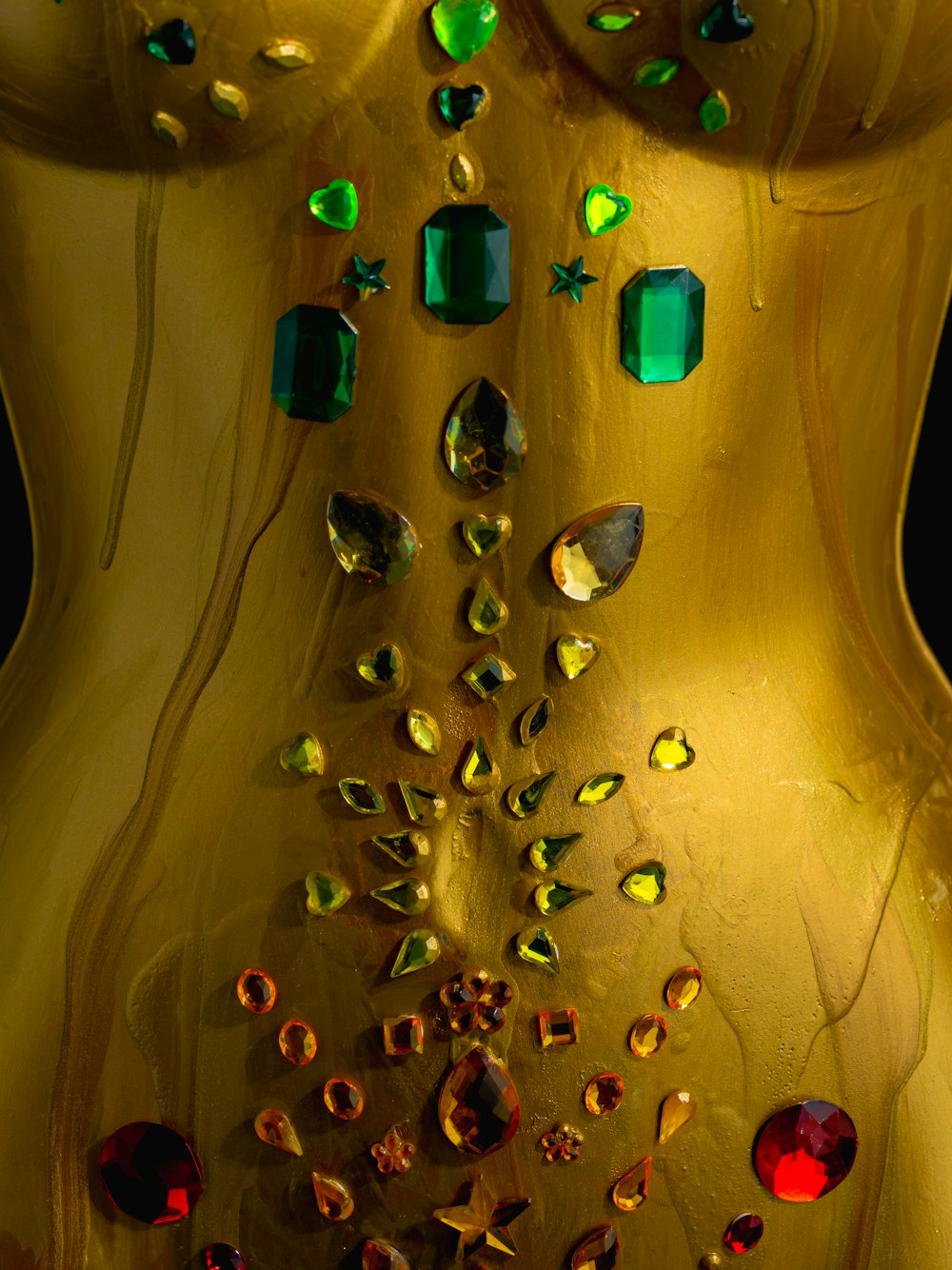 a close up of a gold dress with green and red jewels
