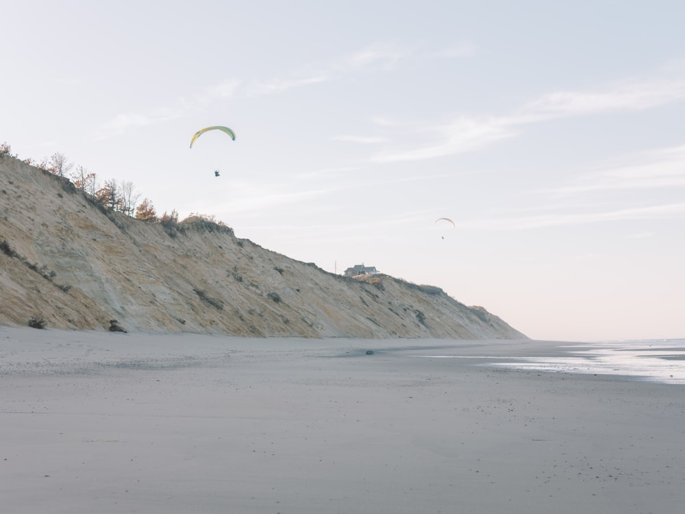 a couple of people flying kites on top of a sandy beach
