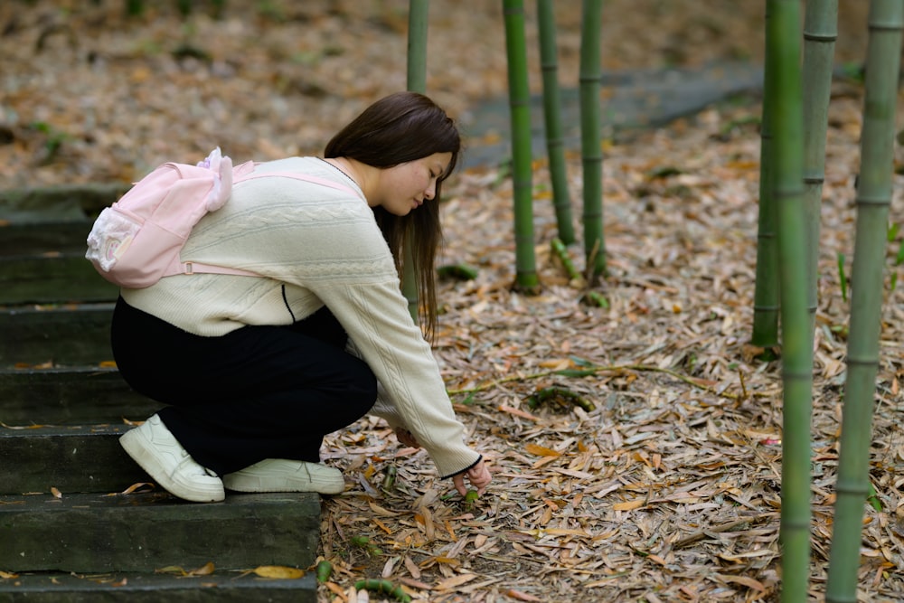 a woman kneeling down in front of a bamboo tree
