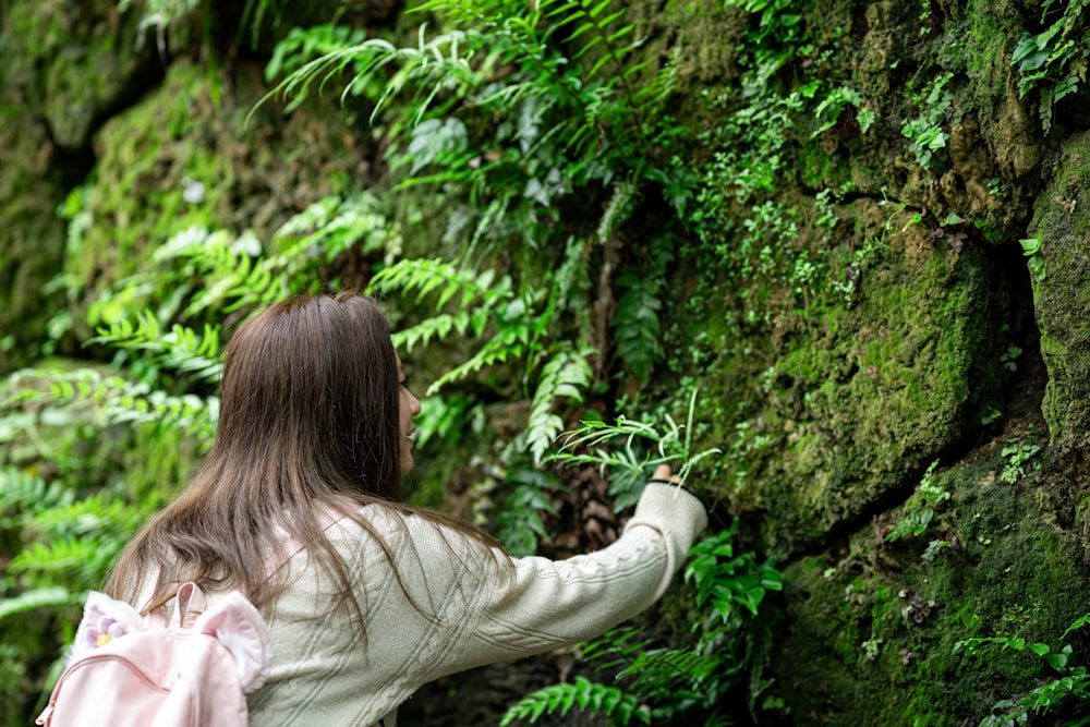 a woman with a pink backpack is looking at a mossy wall