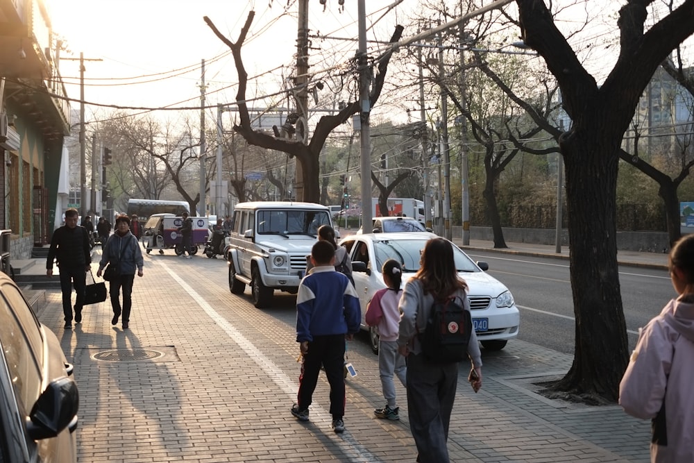 a group of people walking down a street next to parked cars