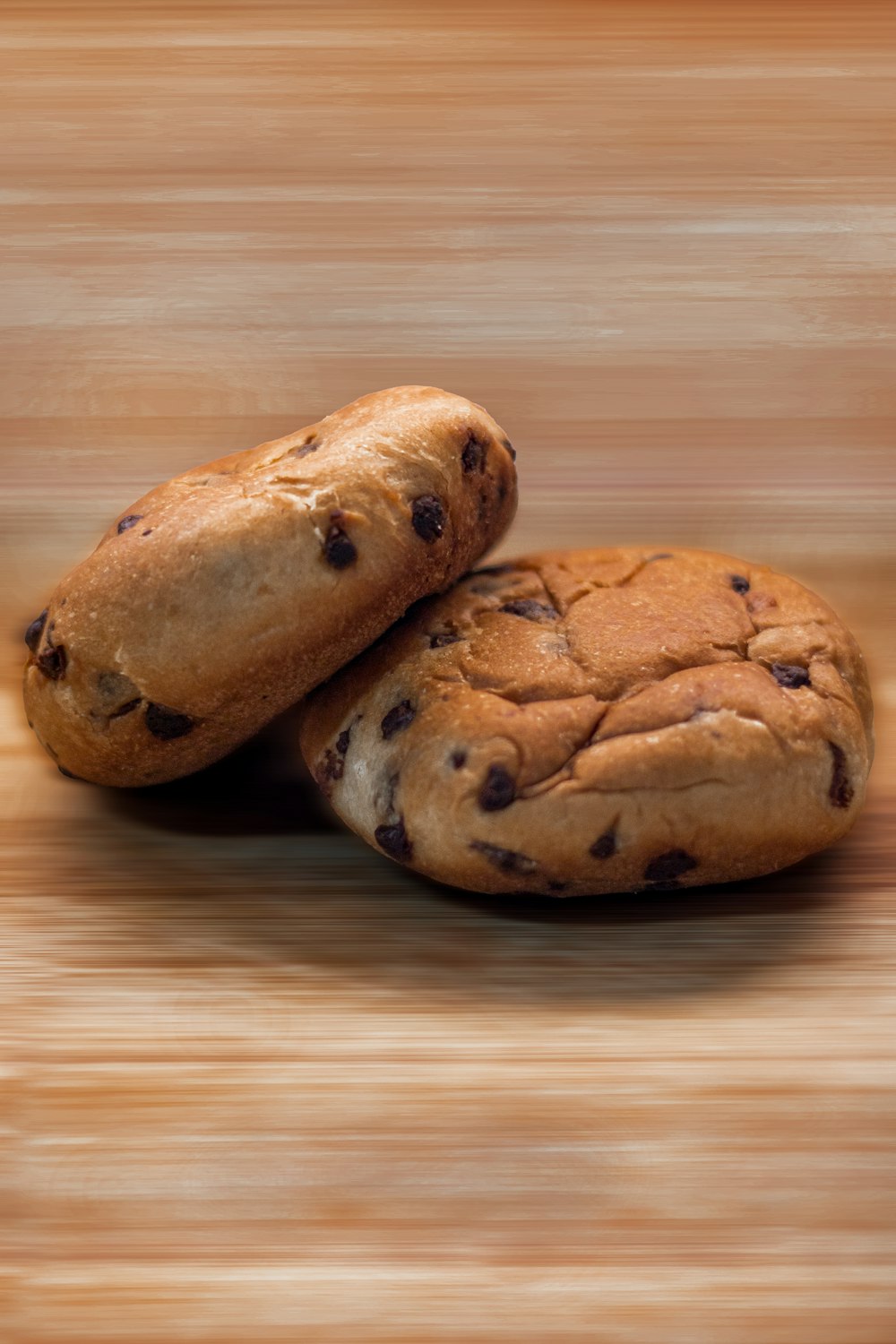 two chocolate chip cookies sitting on top of a wooden table