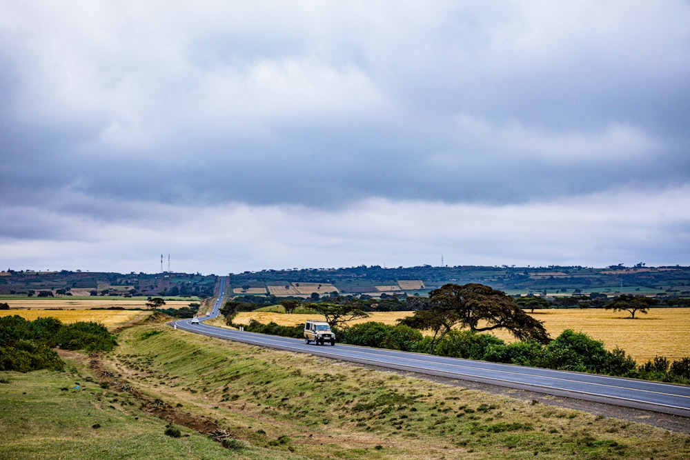 a car driving down a country road under a cloudy sky