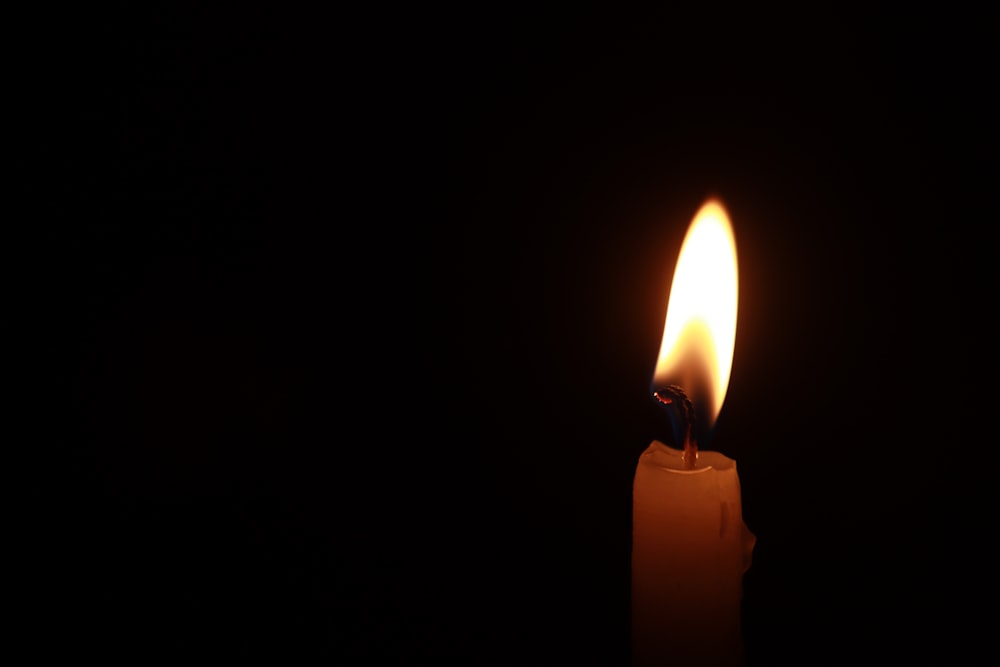 a lit candle in the dark with a black background