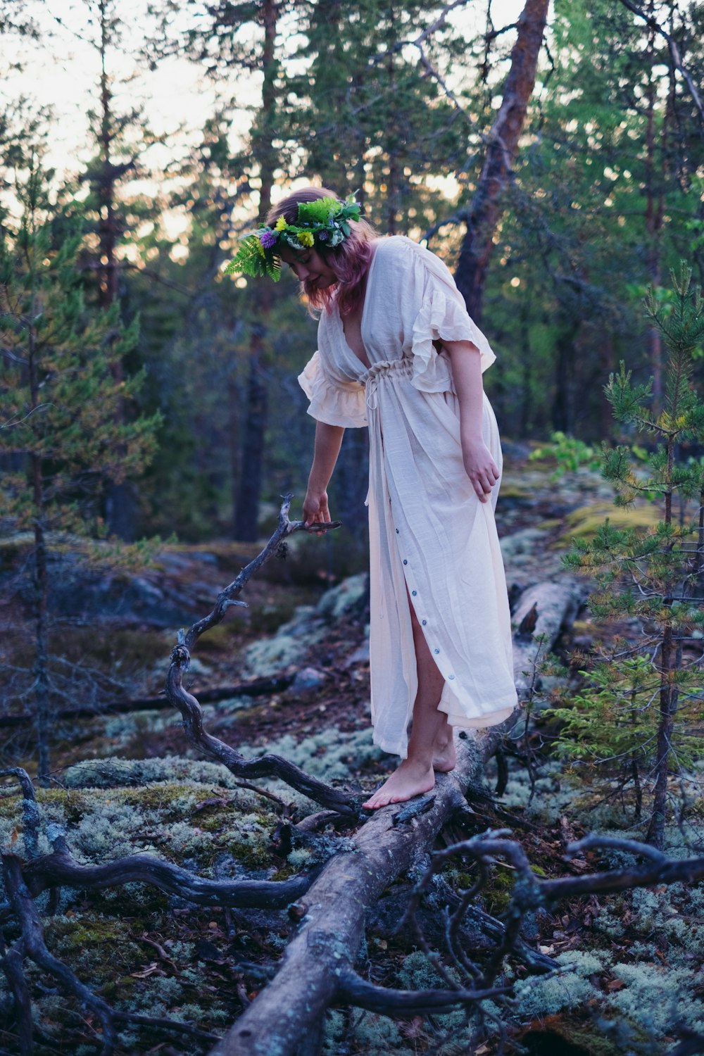 a woman in a white dress walking across a forest