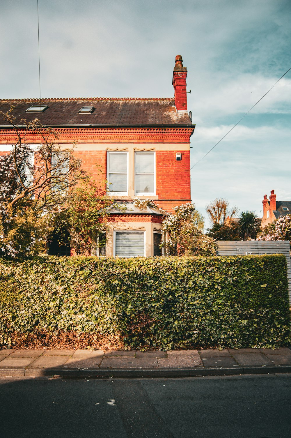 a red brick house with a tall hedge in front of it