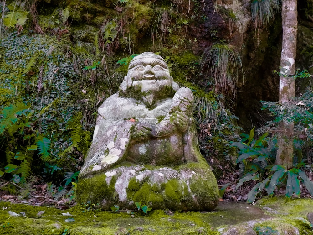 a statue of a man sitting in the middle of a forest