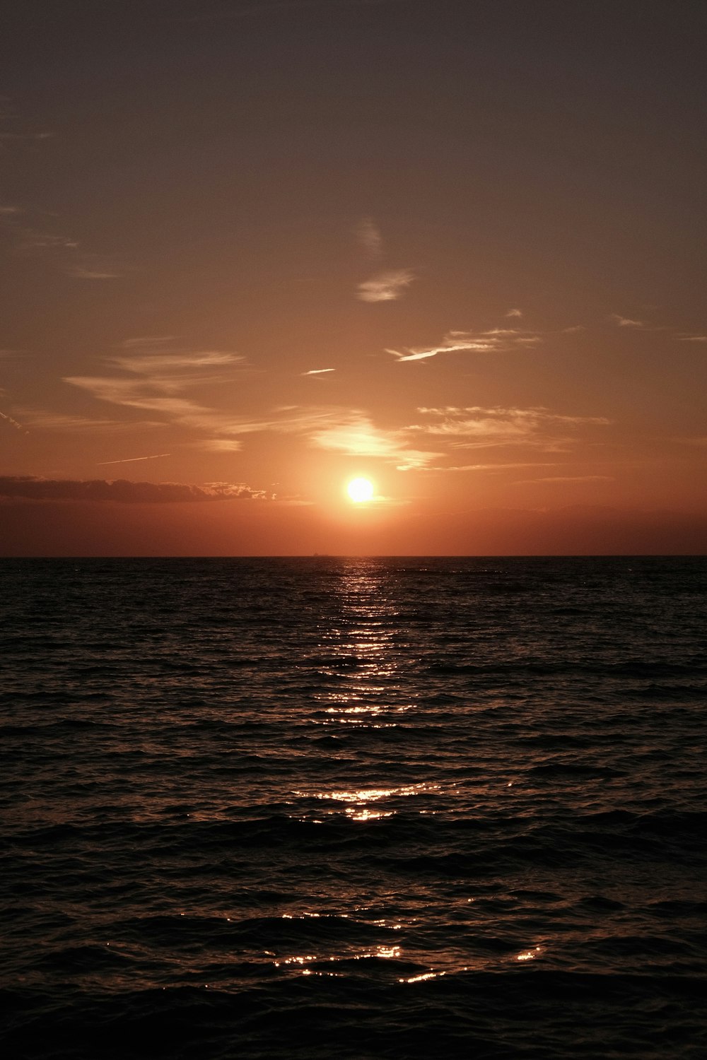 the sun is setting over the ocean on a cloudy day