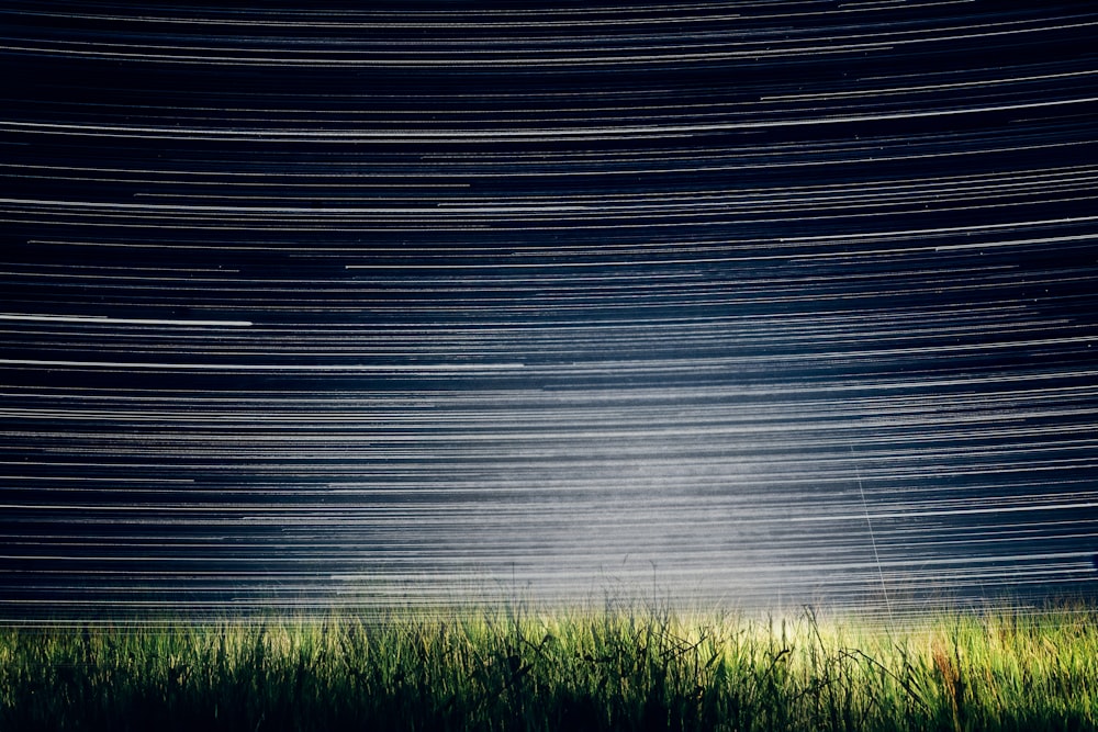 a grassy field with a star trail in the sky