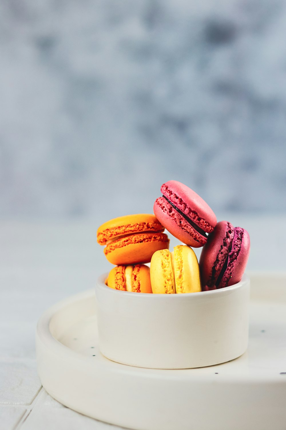 a white bowl filled with colorful macaroons on top of a table