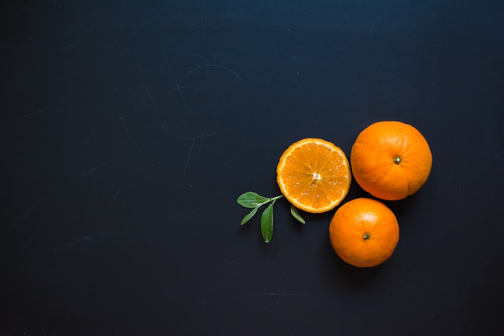 three oranges with leaves on a black surface