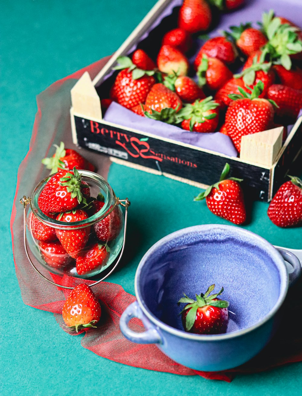 a box of strawberries next to a bowl of strawberries