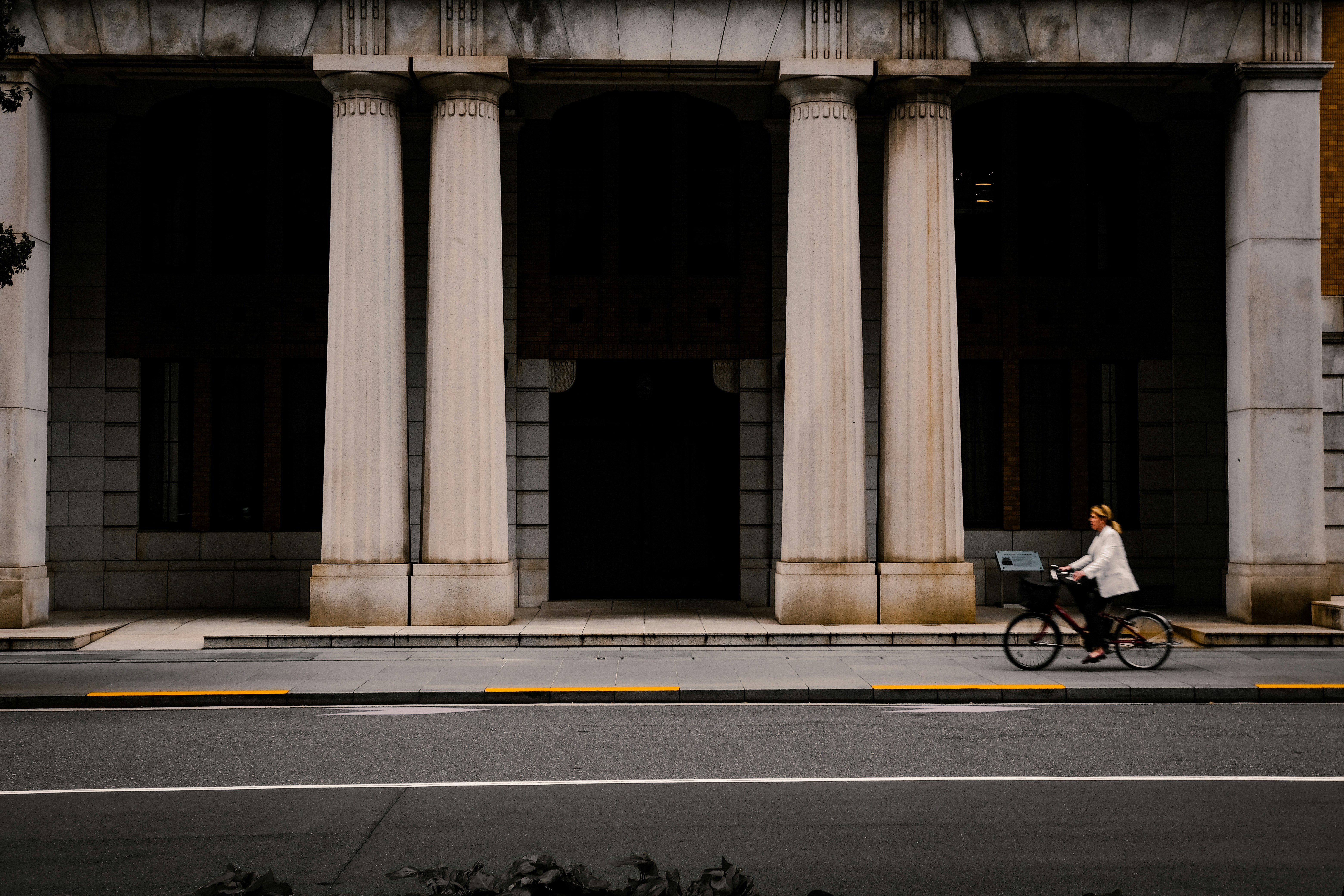 a woman riding a bike down a street past a tall building, a day off in Marunouchi Tokyo Japan