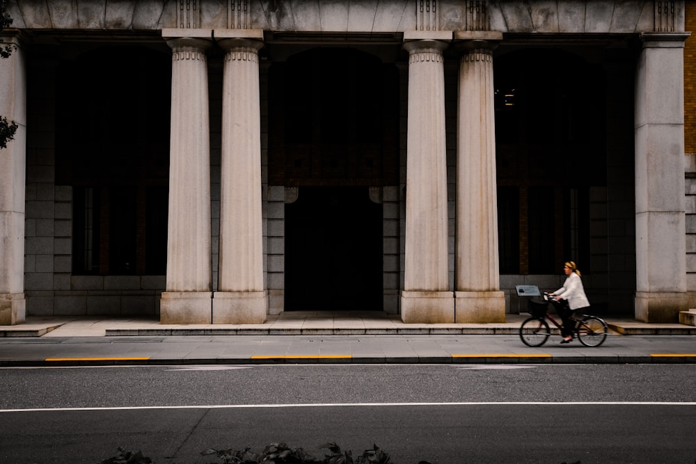 a woman riding a bike down a street past a tall building