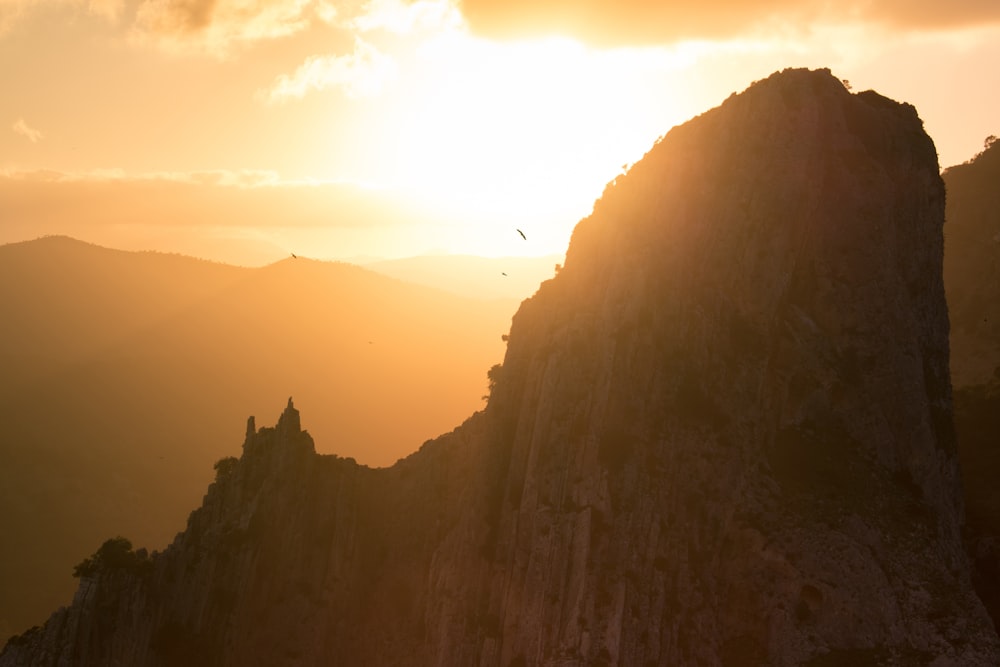 a bird flying over a mountain at sunset