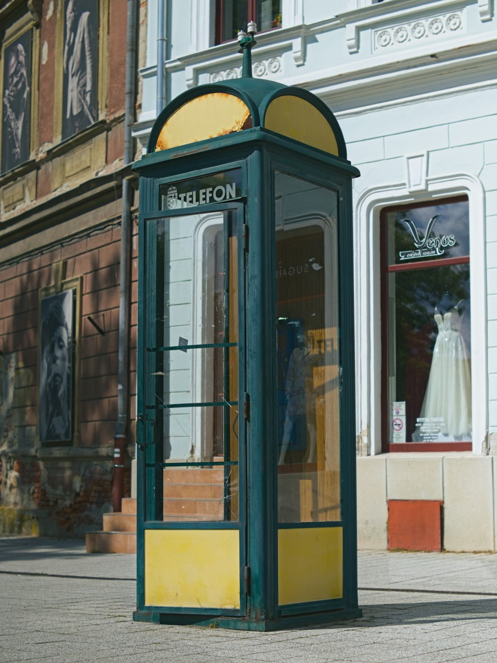 a green and yellow phone booth sitting on the side of a street