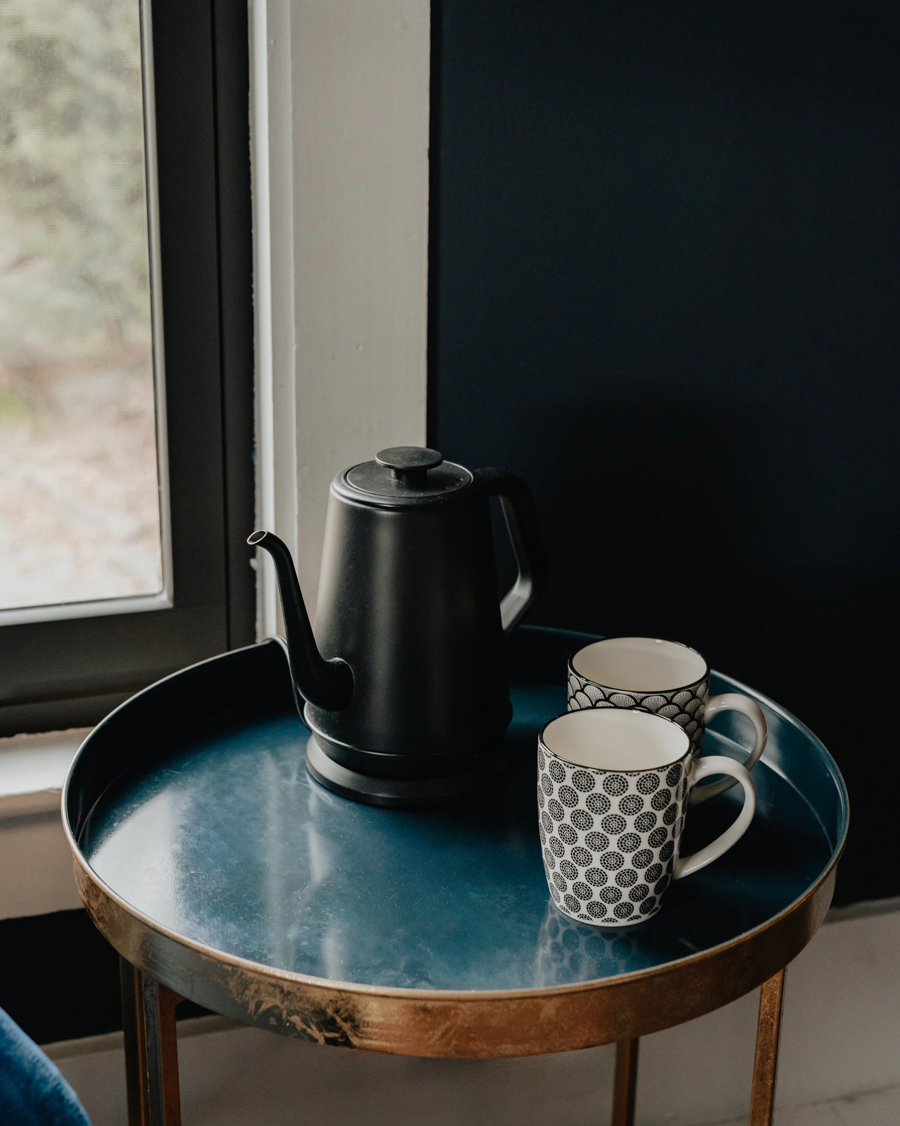 Ceramic mugs beside a dark tea kettle in a quiet serving scene