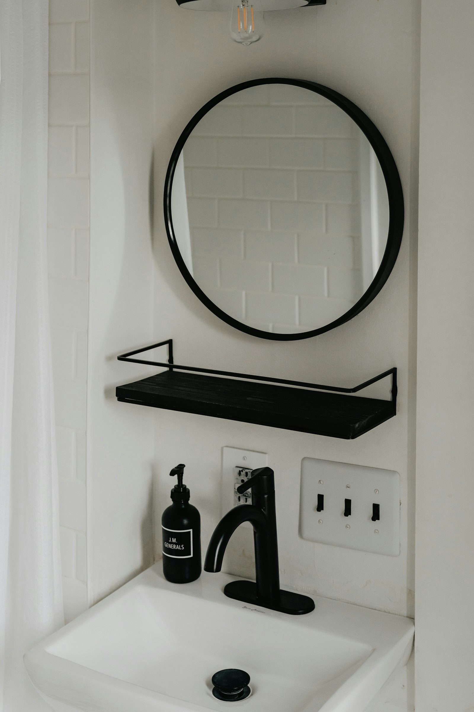 A white sink niche with a round black mirror, black shelf and black faucet