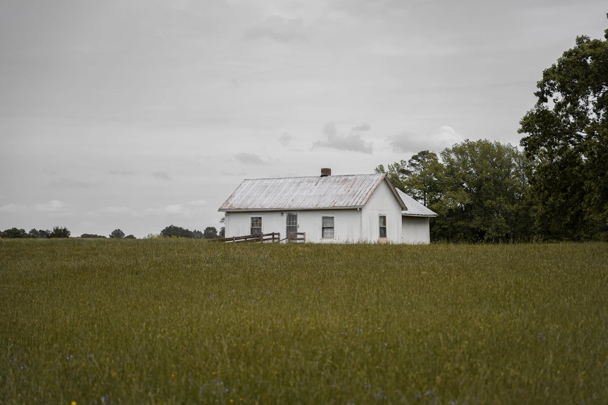 White farmhouse exterior with black roof surrounded by trees on a slope