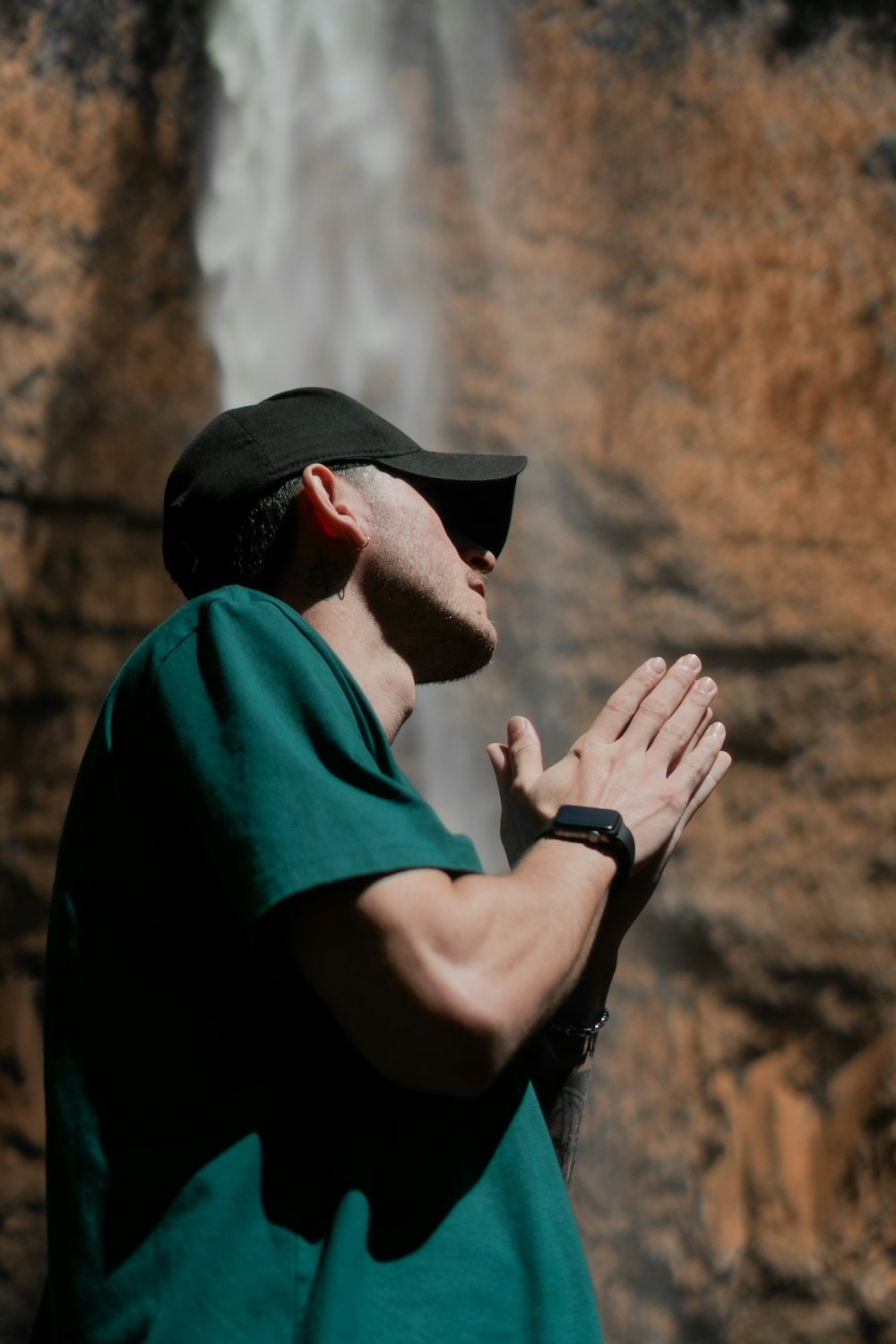 a man standing in front of a waterfall with his hands together