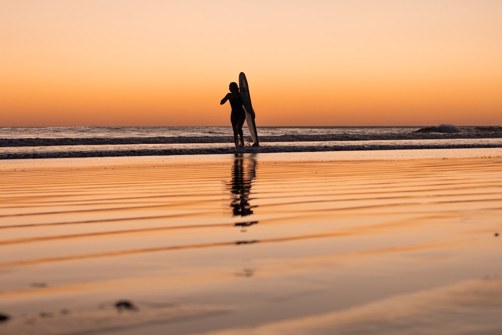 Un hombre sosteniendo una tabla de surf de pie en la parte superior de una playa