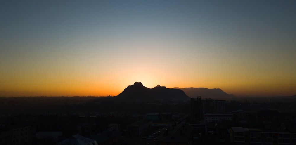 the sun setting over a city with a mountain in the background