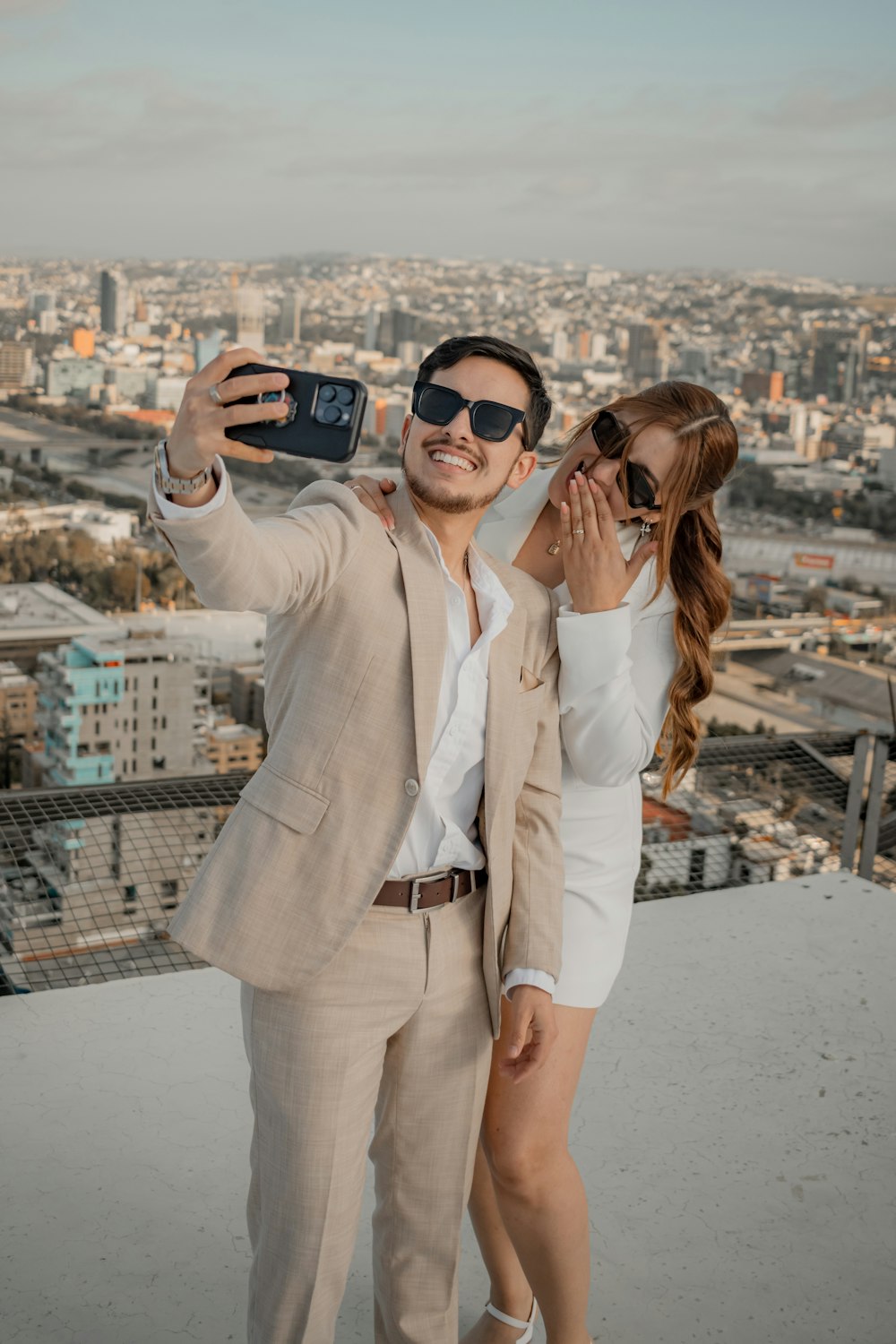 a man and woman taking a selfie on top of a building