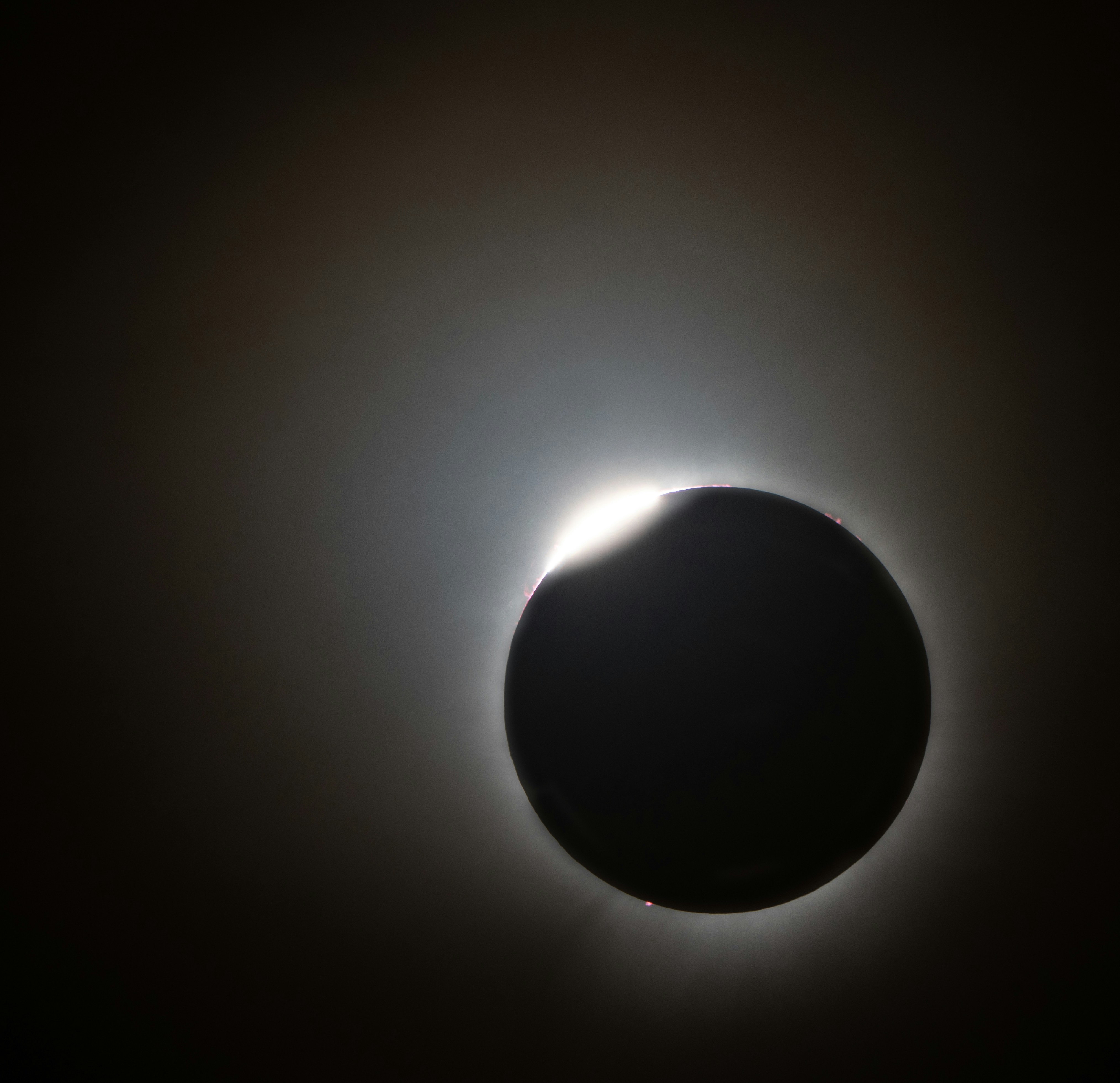 Total solar eclipse diamond ring effect, corona visible against pitch black sky with golden light burst