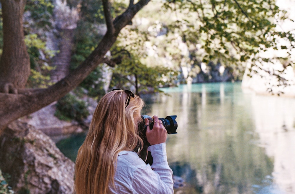 a woman taking a picture of a lake with a camera