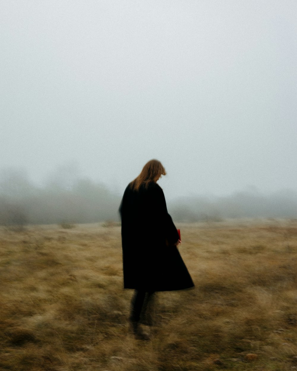 a woman in a black coat walking through a field