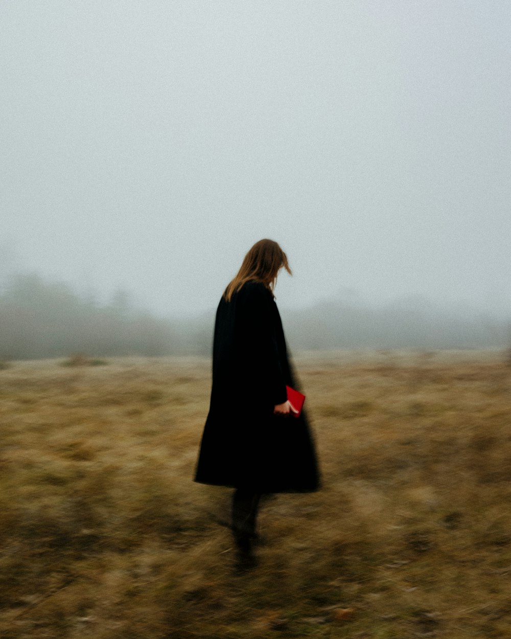 Eine Frau in einem schwarzen Mantel geht durch ein Feld