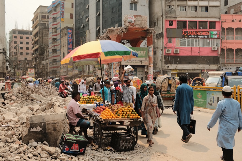 a group of people walking down a street next to a pile of fruit