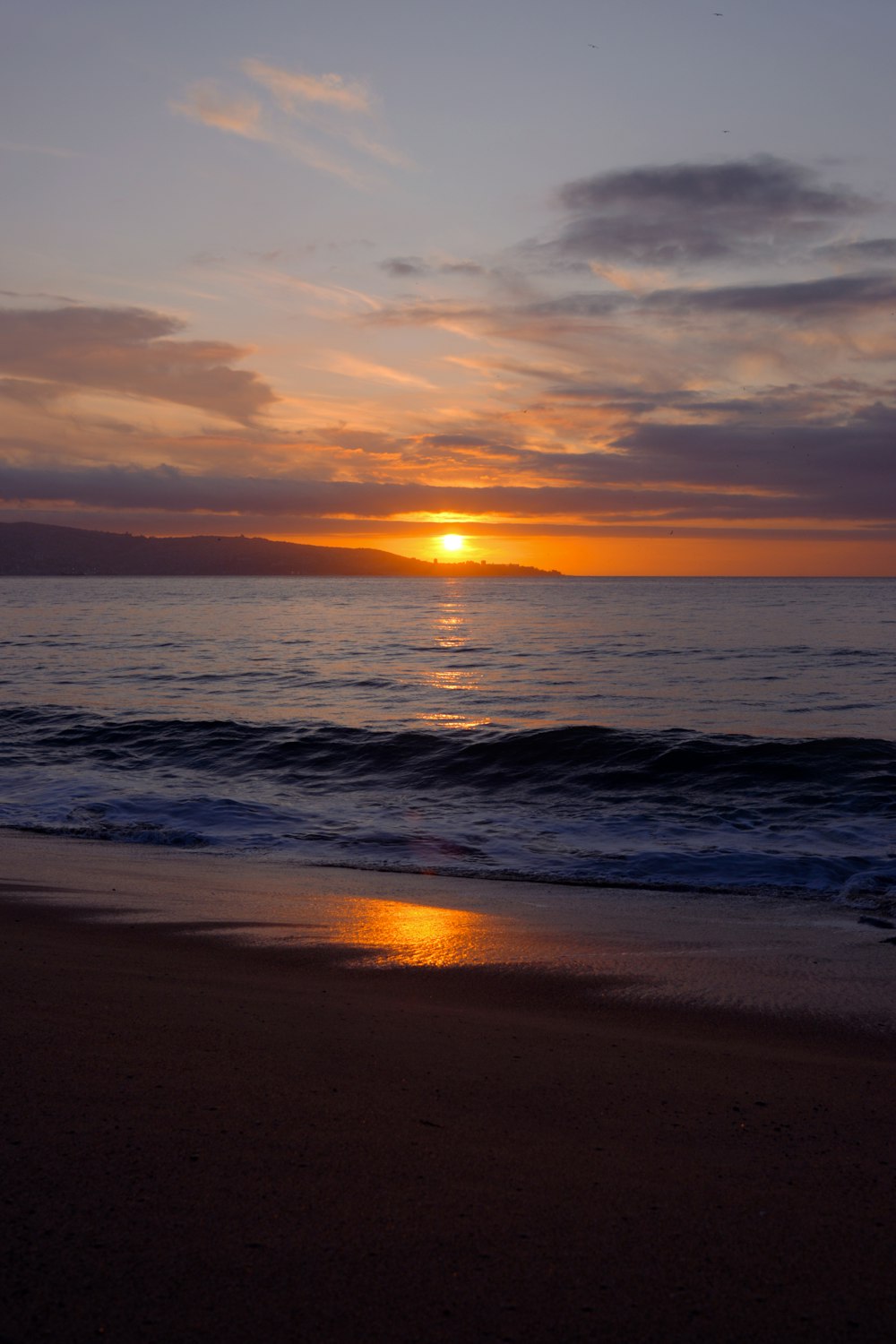 the sun is setting over the water on the beach