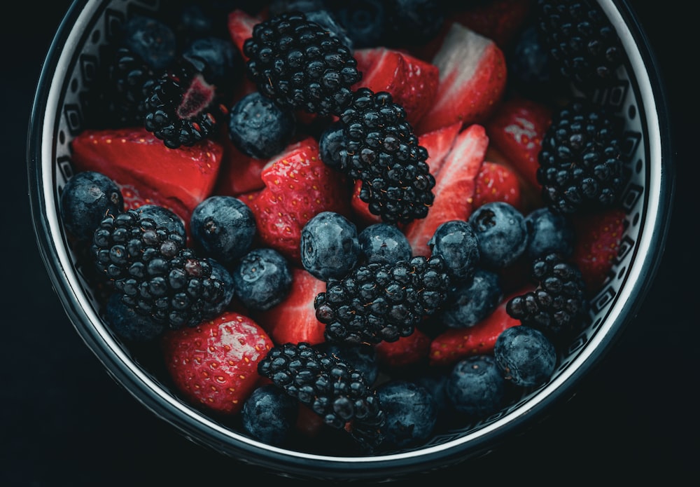 a bowl of berries and strawberries on a black background