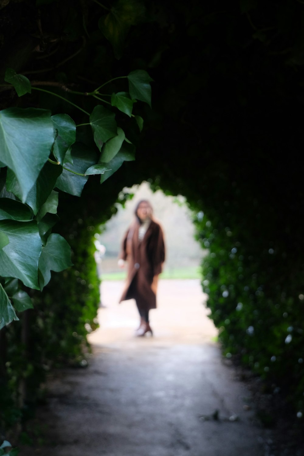 a woman is walking through a tunnel of green leaves